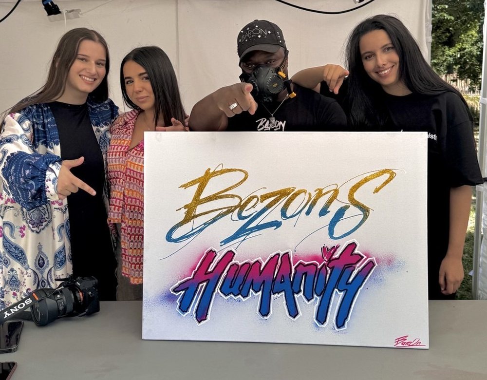 Quatre bénévoles de Bezons Humanity posant avec la toile aux couleurs de l'association, réalisée en direct lors d'un événement